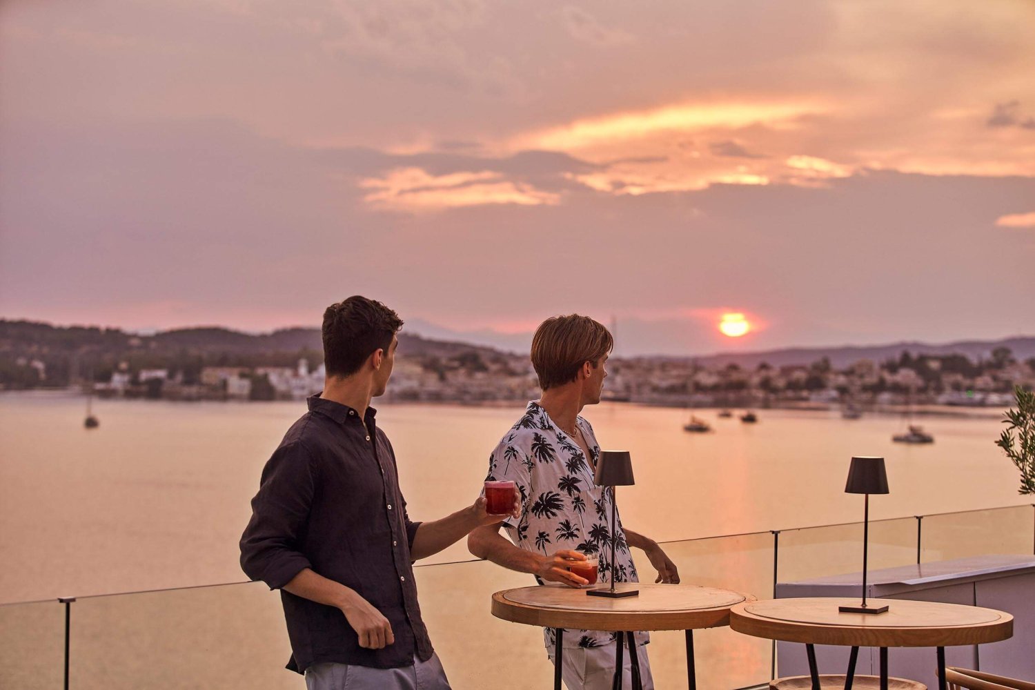 Two men drinking cocktails on a balcony looking out to the sea