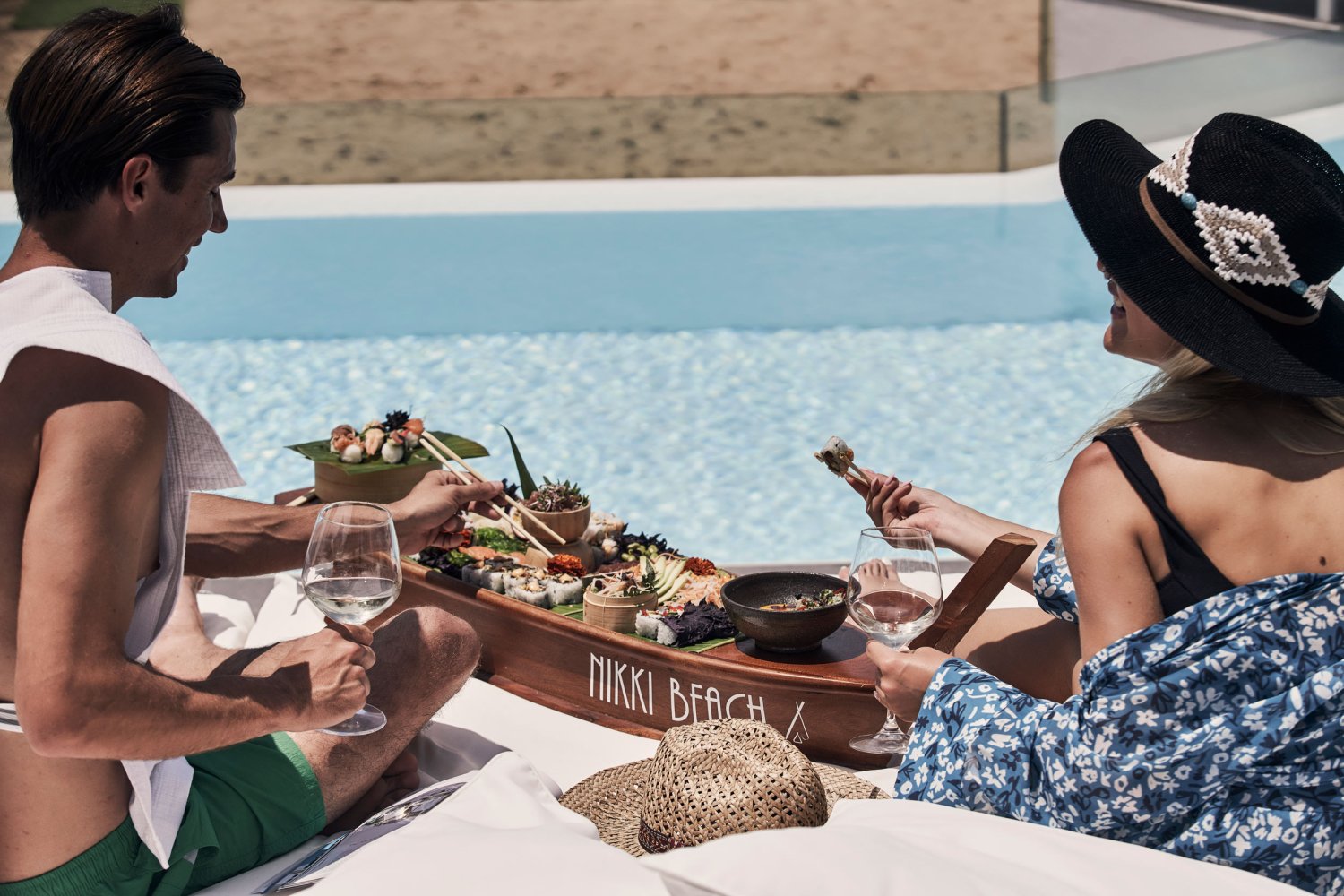 Two people sitting on the edge of the pool, eating Nikki beach platter