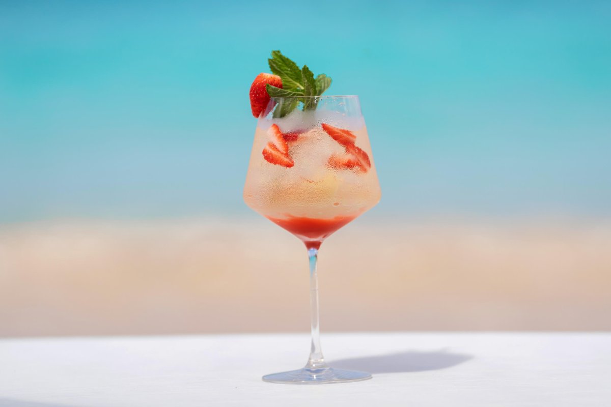 Wide angle shot of a cocktail in focus with the sand and sea out of focus in the background