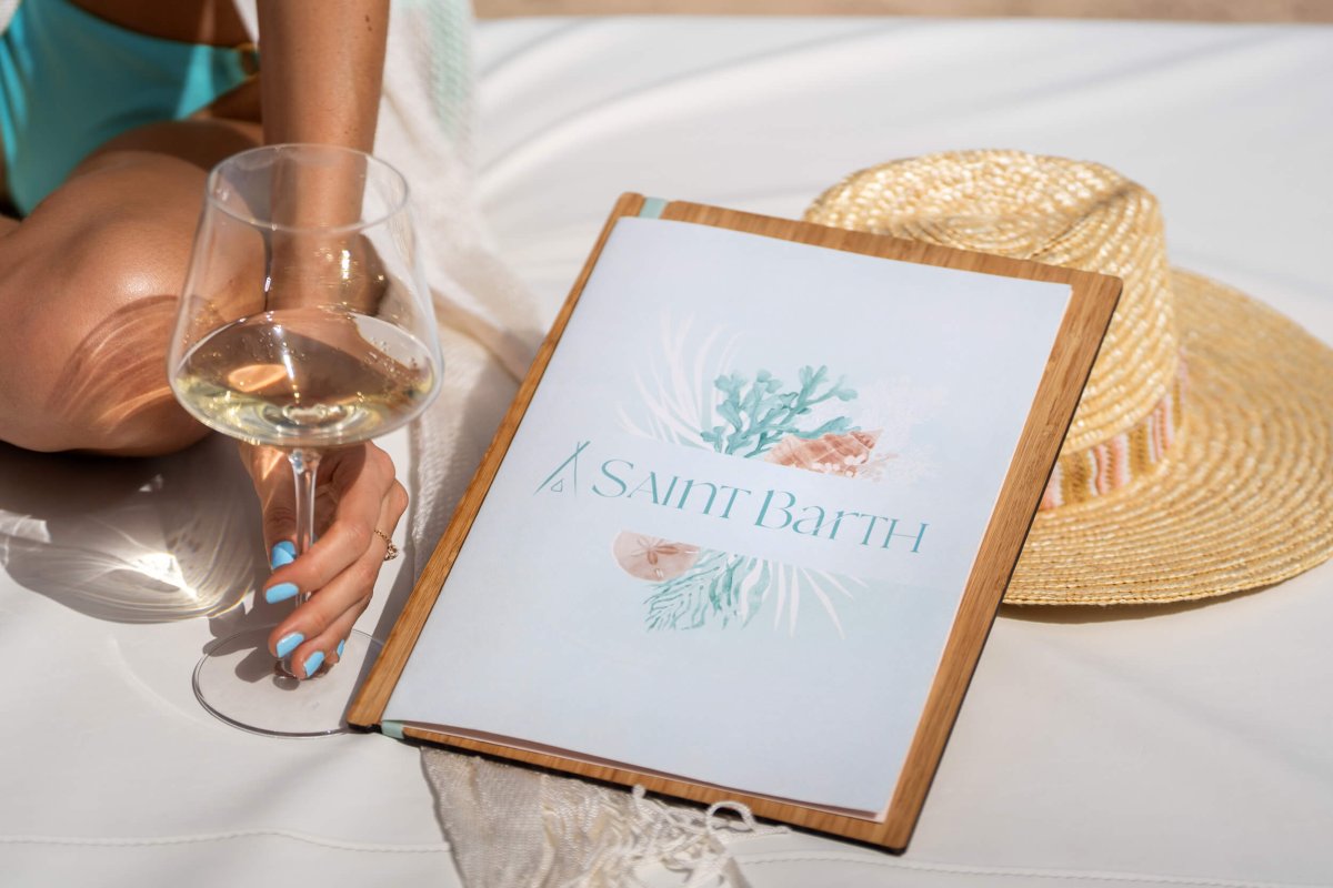 Nikki Beach Saint Barch menu sitting next to a woman holding a glass of white wine