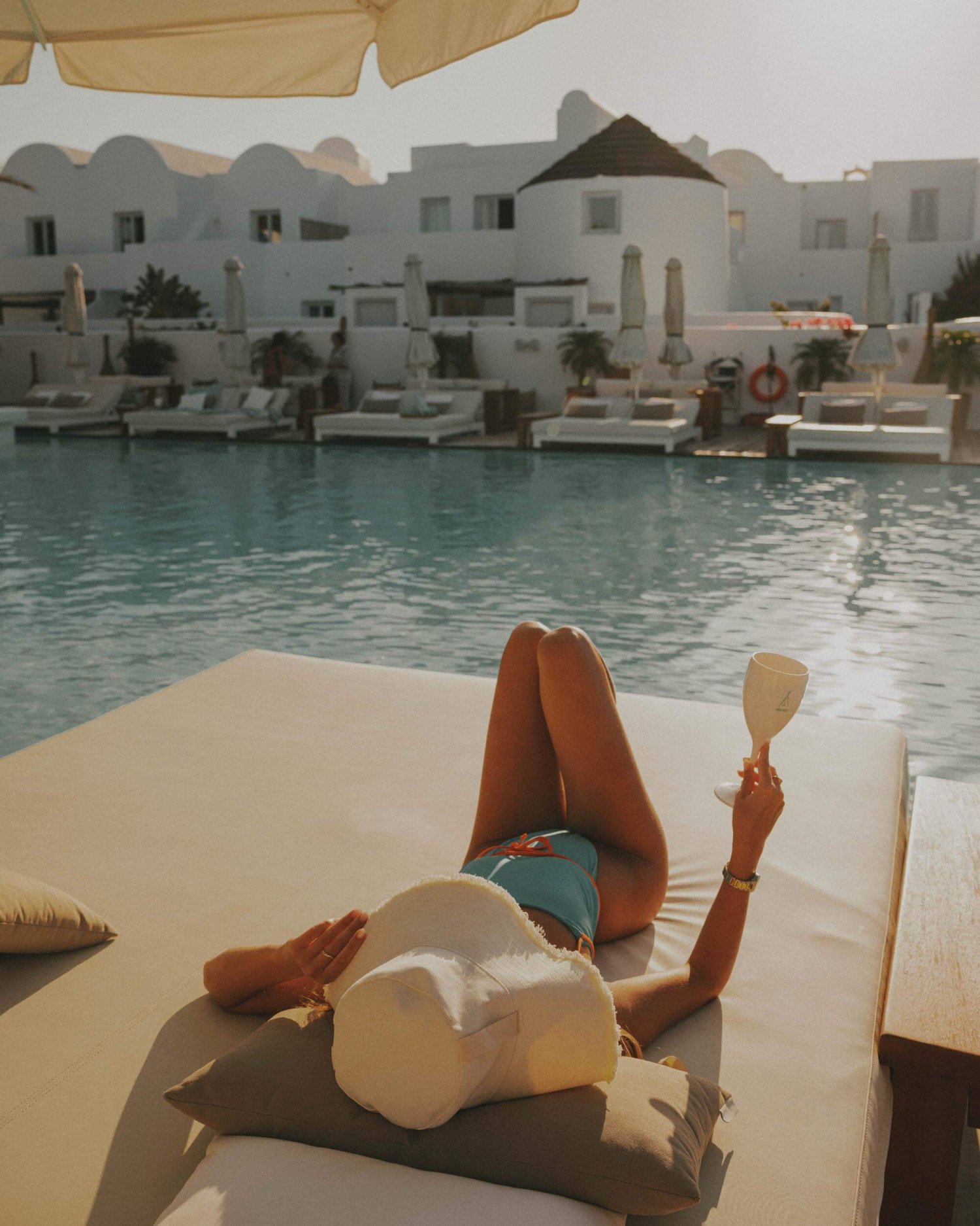 A women lying on a sun bed next to the pool, holding a Nikki Beach wine glass