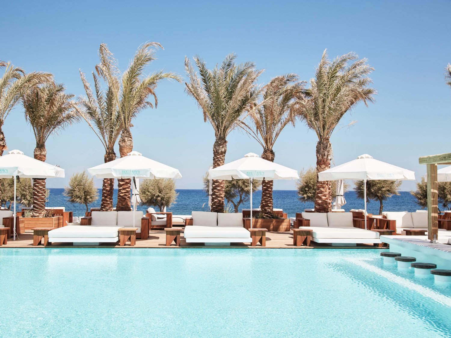 Wide shot of the resort pool and palm trees at Nikki Beach Santorini