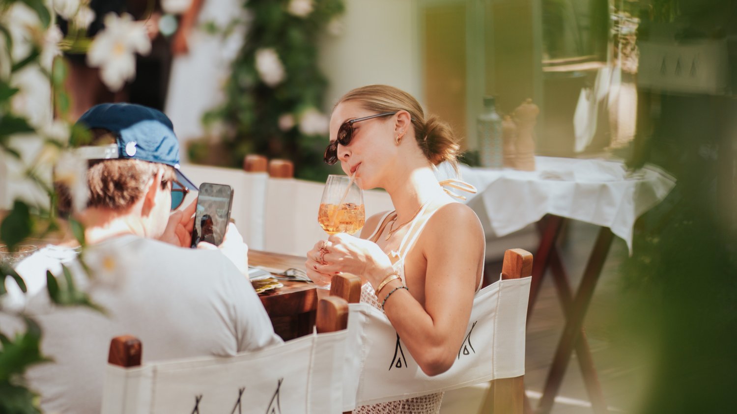 Women posing, drinking through a straw while her partner takes a photo on his phone