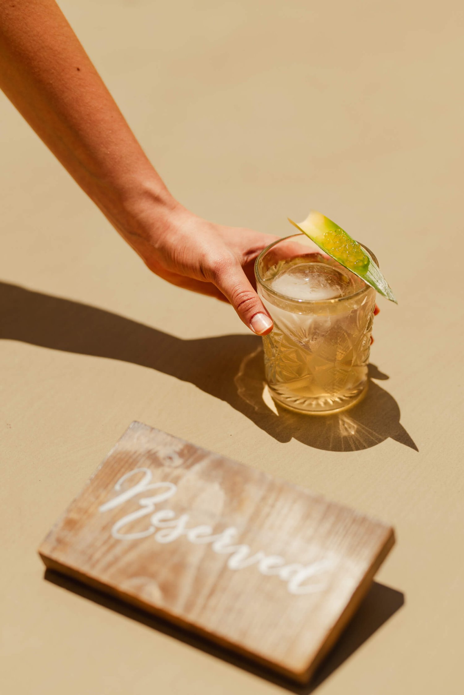 A hand grabbing a cocktail next to a wooden reserved sign