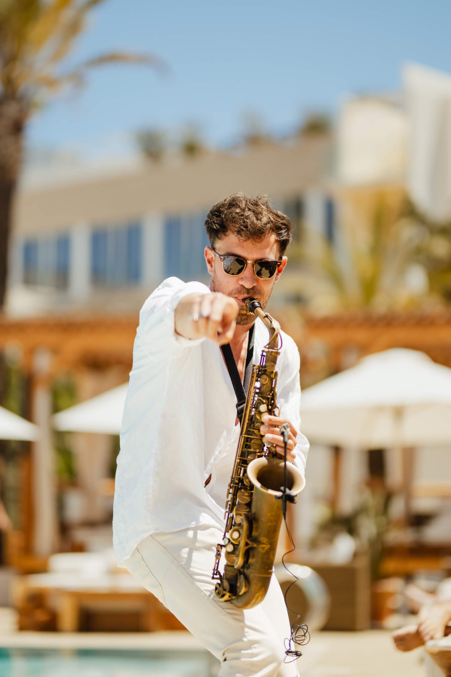 Man in a white shirt playing the saxophone pointing at the camera