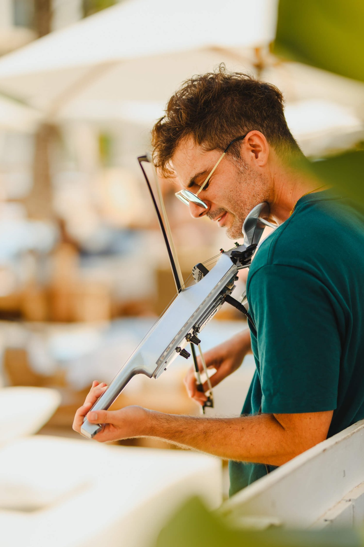 Man in a teal t-shirt playing a white violin