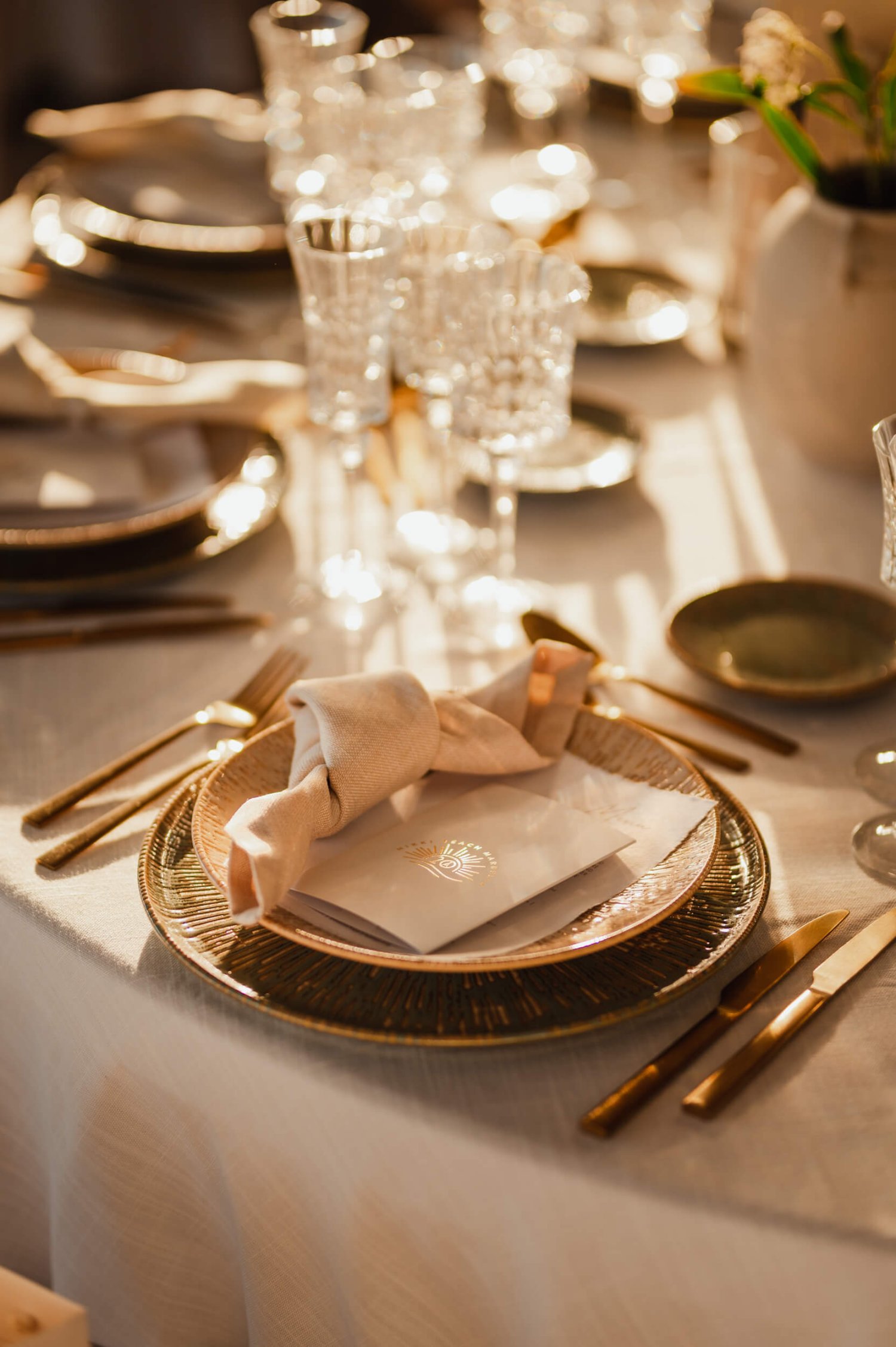 A beautifully laid table with menus and napkins place on top of the plates. Gold cutlery surrounding along with various wine glasses