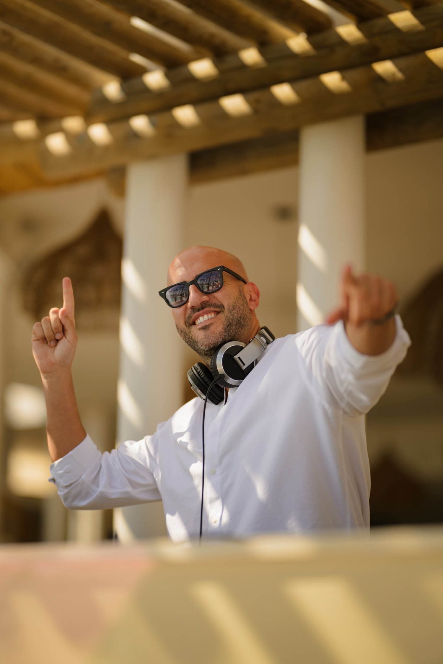DJ Jordi Ruz wearing headphones, smiling and pointing his hands in the air