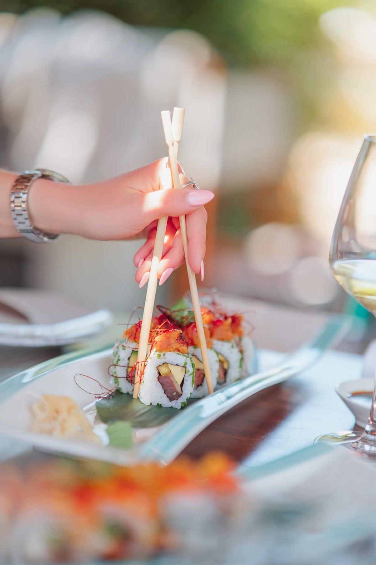 Woman with chopsticks picking up sushi from a plate