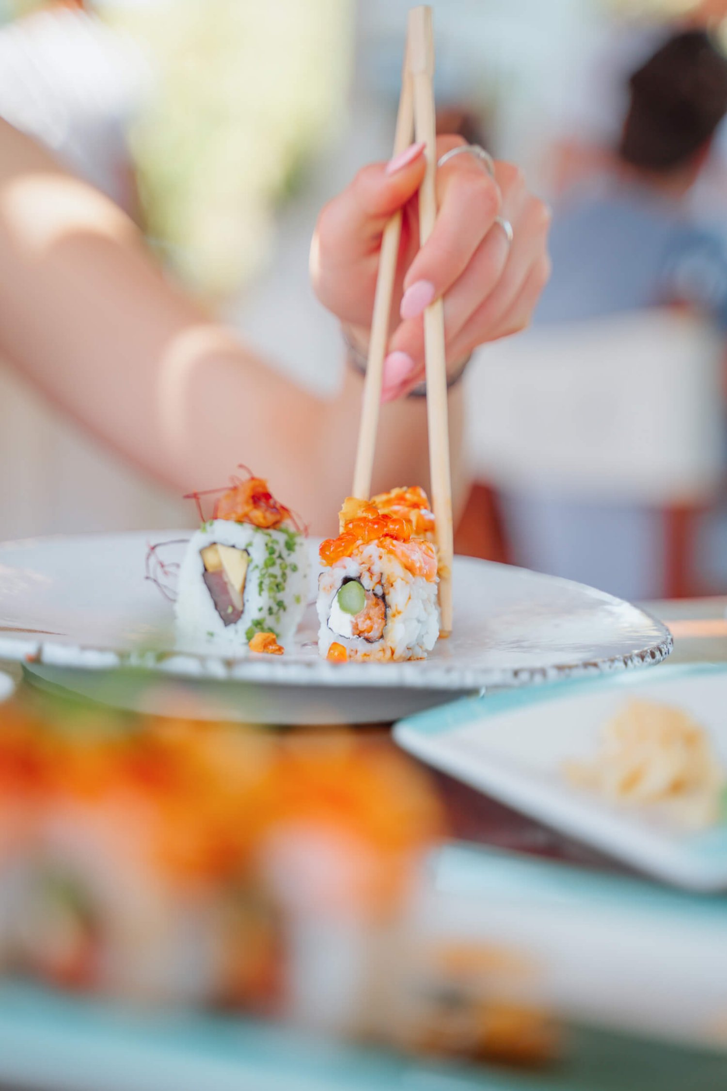 Woman with chopsticks picking up sushi from a plate