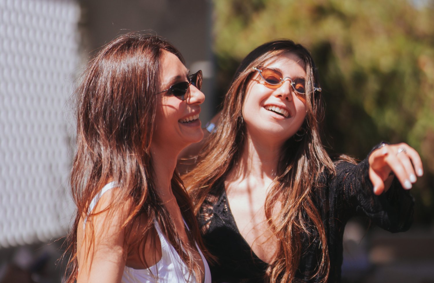 Two women wearing sunglasses, smiling and laughing