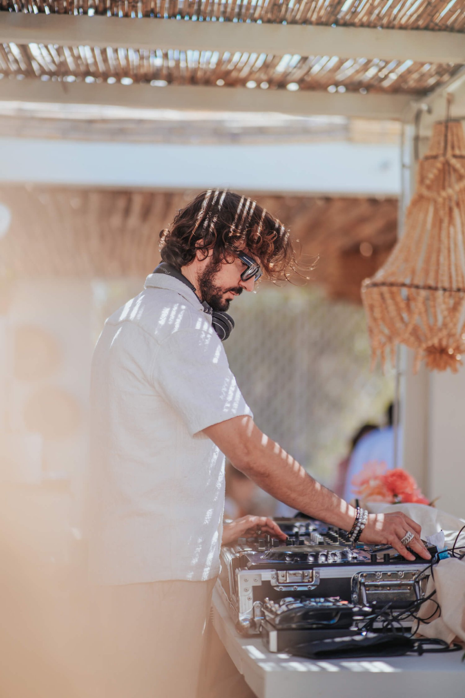 DJ in a white shirt with headphones around his neck on the decks