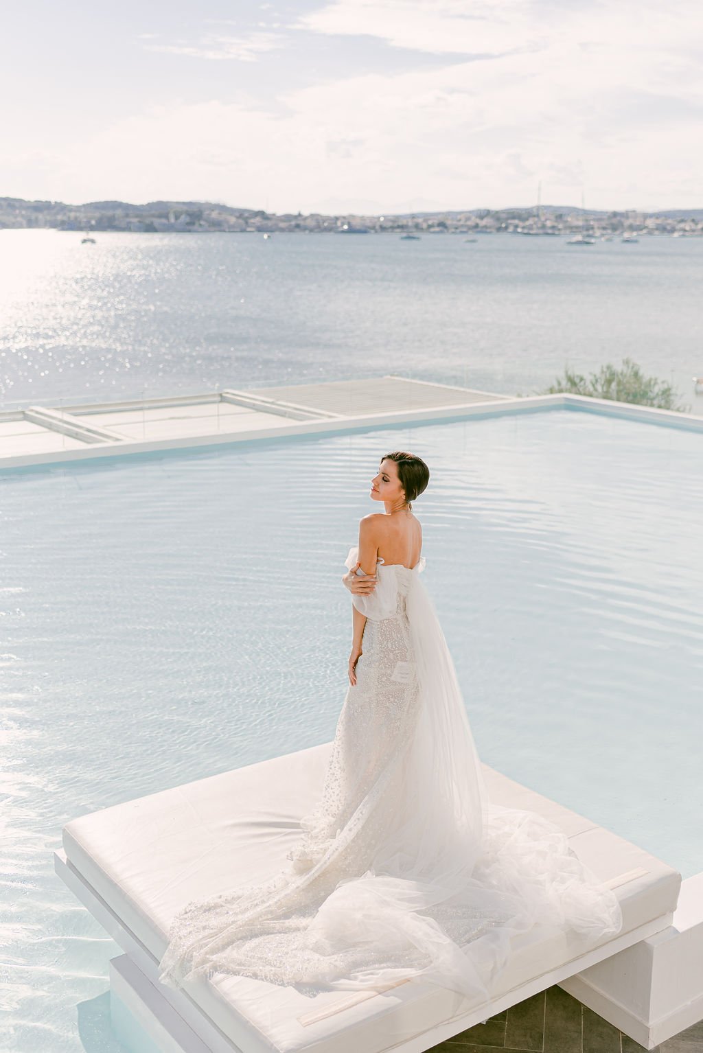 A bride posing on the edge of the pool with the sea in the background