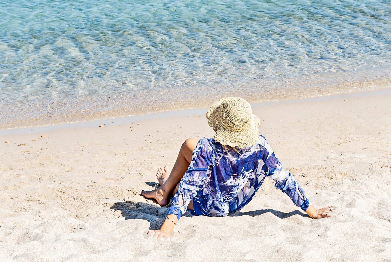 A women in a women had sitting in the sand by the sea