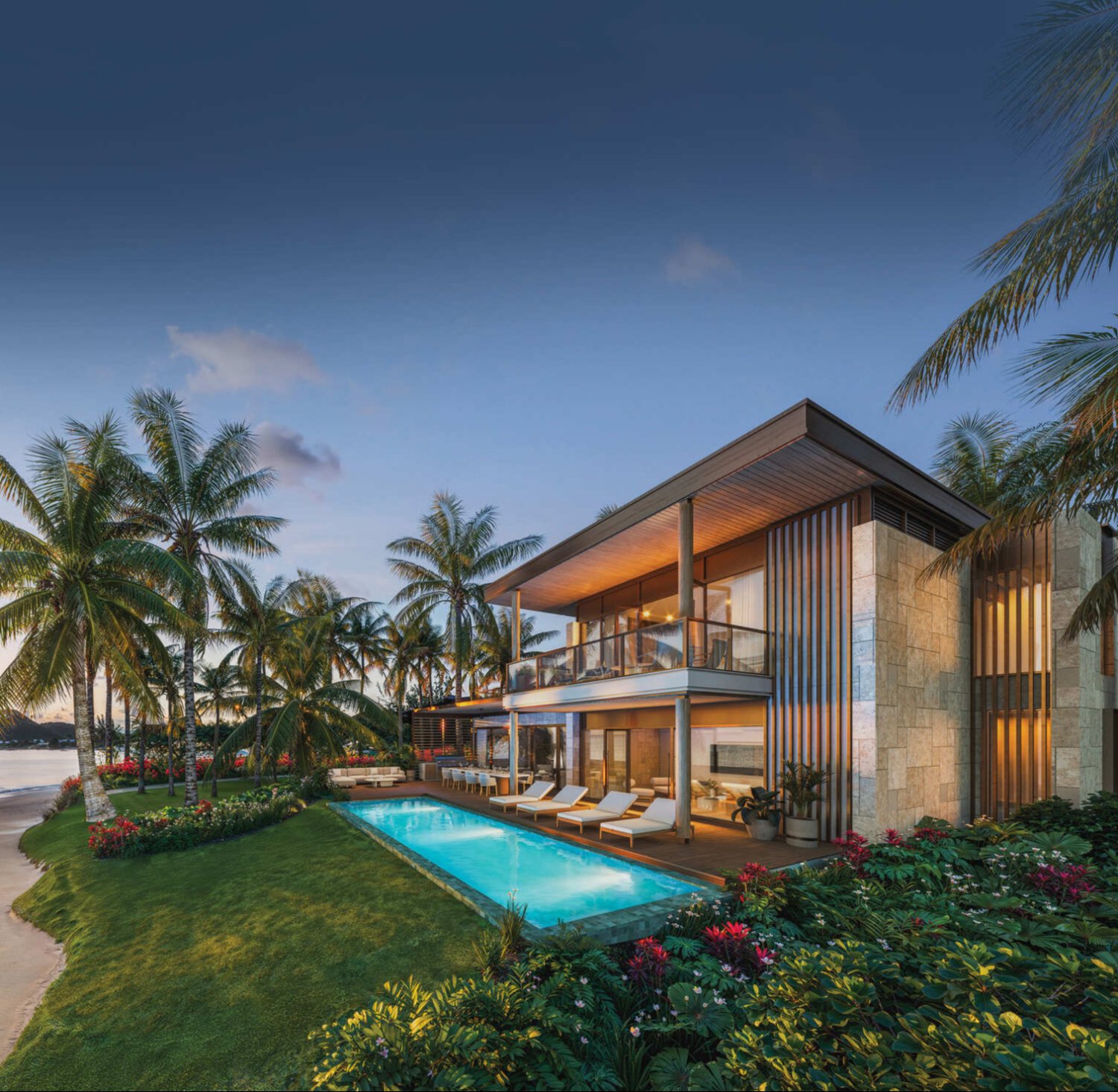 An exterior view of a luxury beachfront villa at Nikki Beach Residences Antigua at sunset. The modern two-story home features large glass windows, a private rectangular pool, and an outdoor lounge area surrounded by tropical palm trees, sitting directly on a sandy beach next to the calm Caribbean Sea