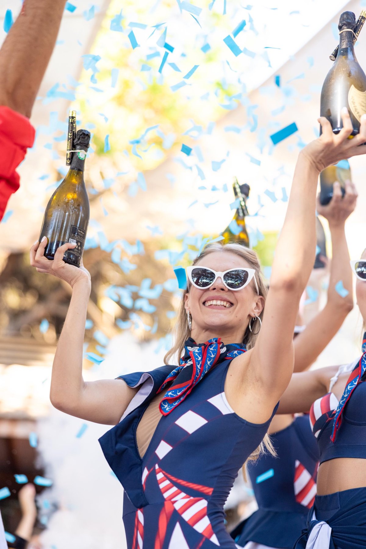 Woman in blue dress holding up some bottles surrounded by confetti