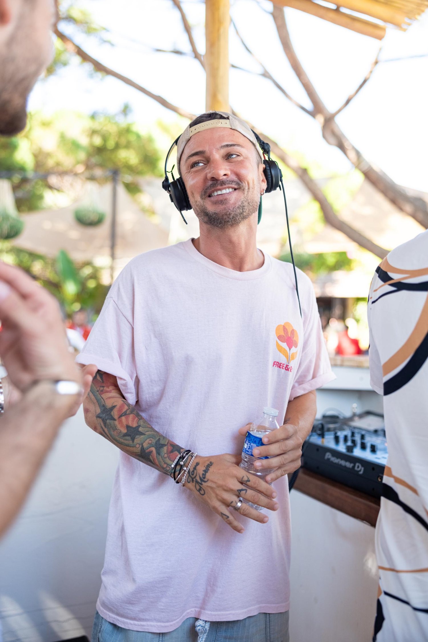 DJ in a light pink t shirt holding a bottle of water smiling at a man
