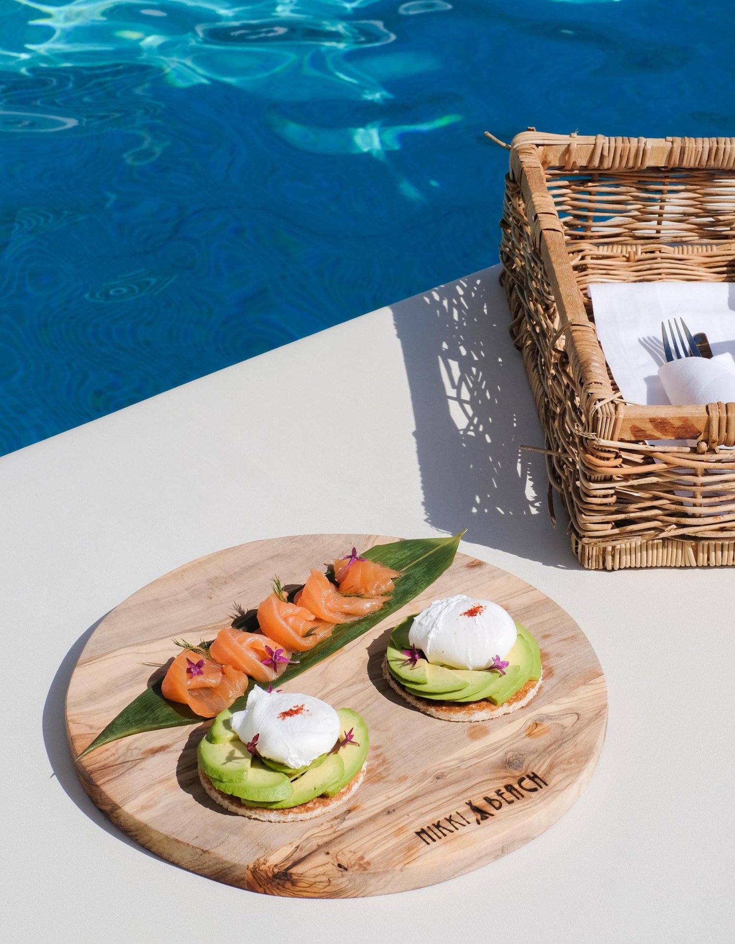 Small salmon and avocado dishes on a round Nikki beach board, placed near the poolside