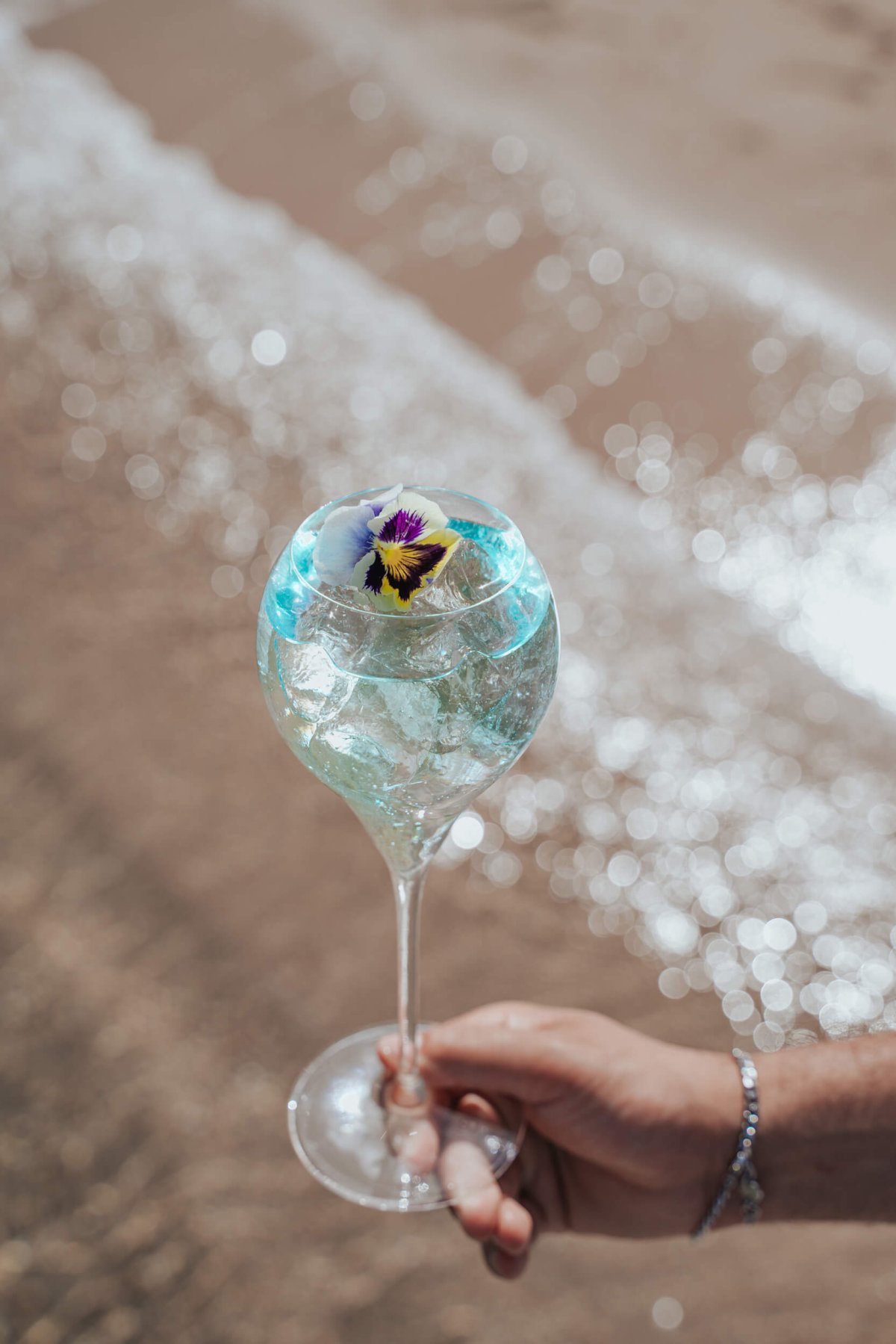 Royal Emerald Spritz held in a glass above the sand