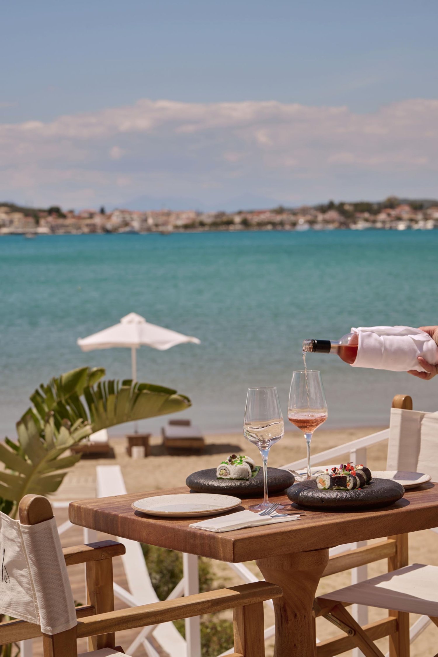A waiter pouring glasses of rosé at a small table on the beach front