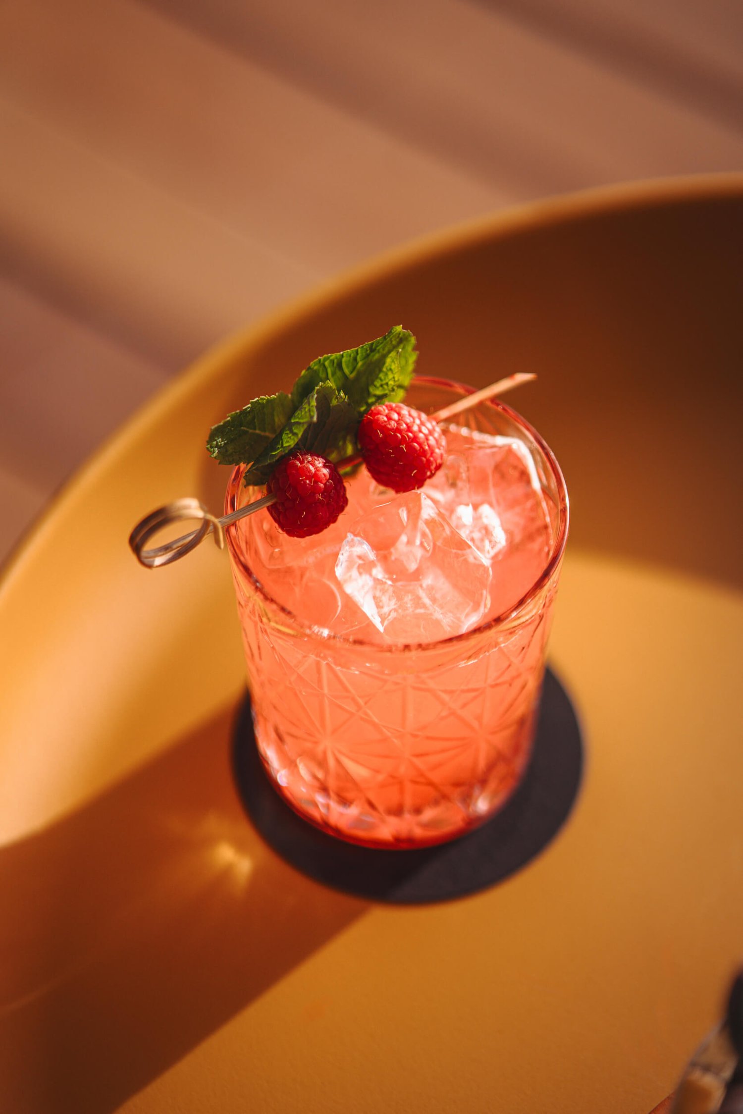 Top view of a pink cocktail with raspberries and mint garnish