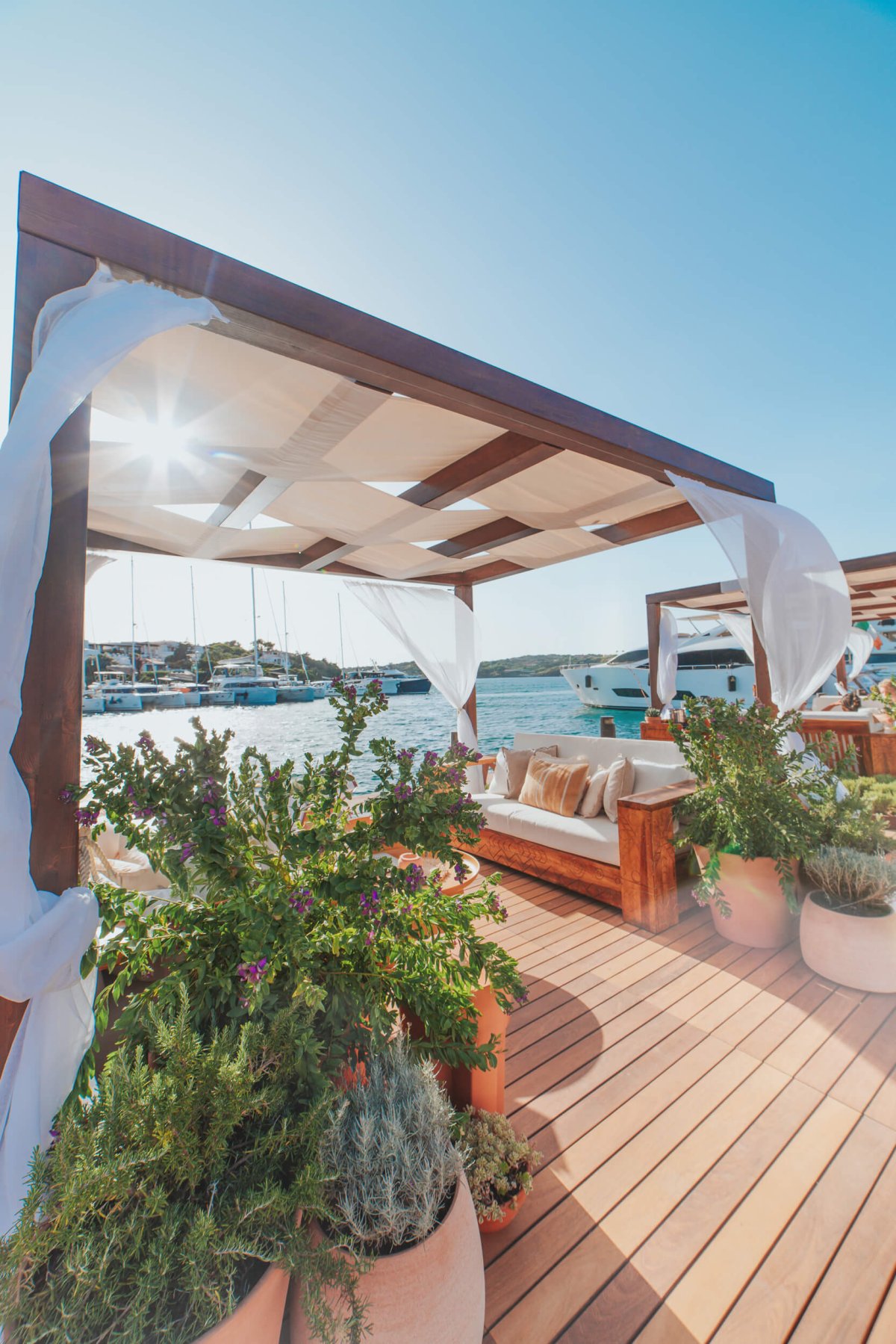 Pergola with white sheets next to the harbour surrounded by potted plants