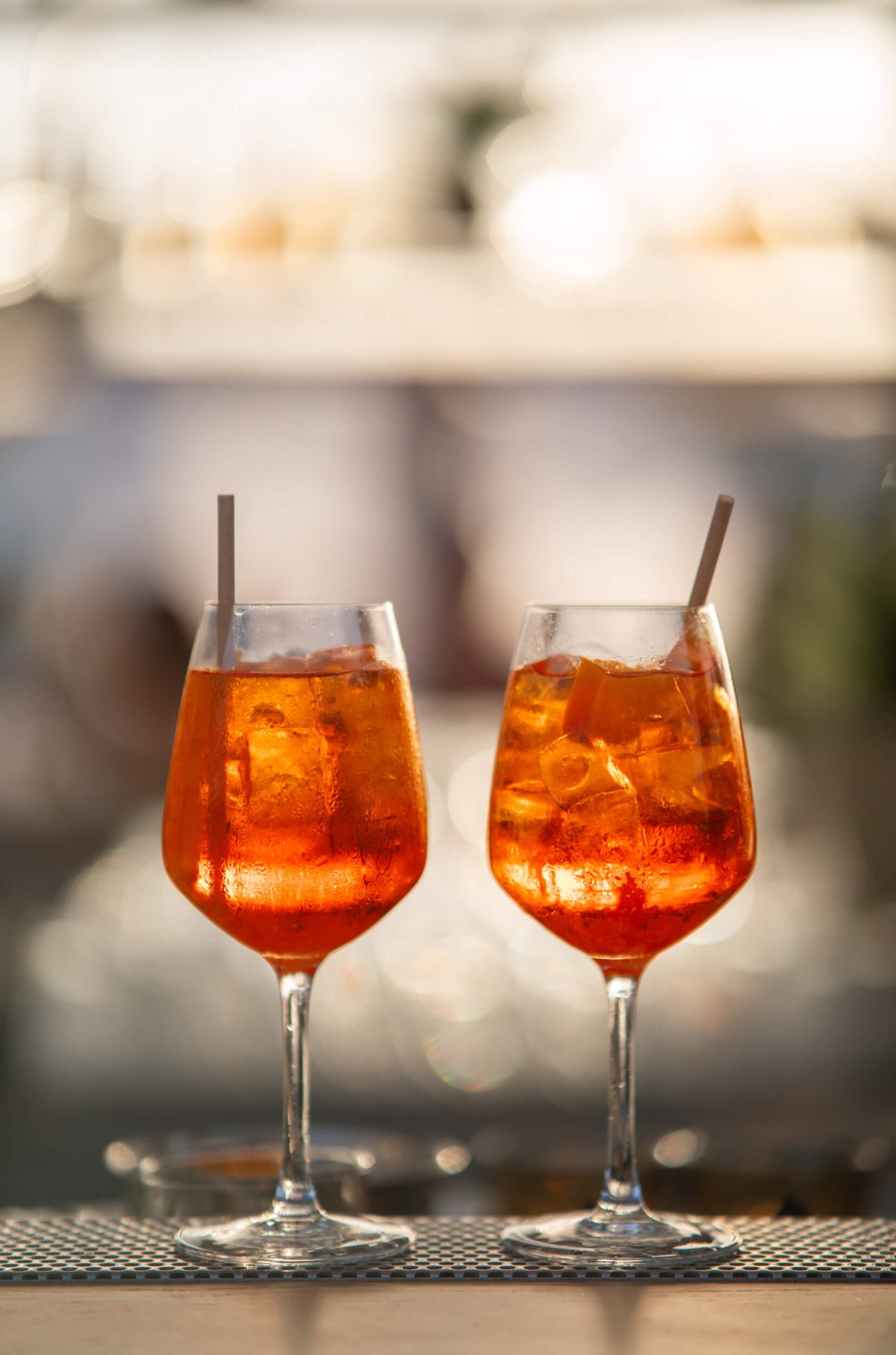 Two Aperol spritz drinks with straws coming out of the top of the glasses