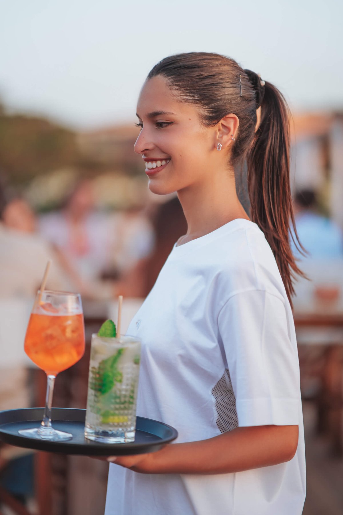 Smiling waiter in a white T-shirt holding a tray of cocktails